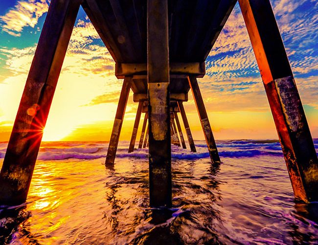 image of the beach under a pier at sunset