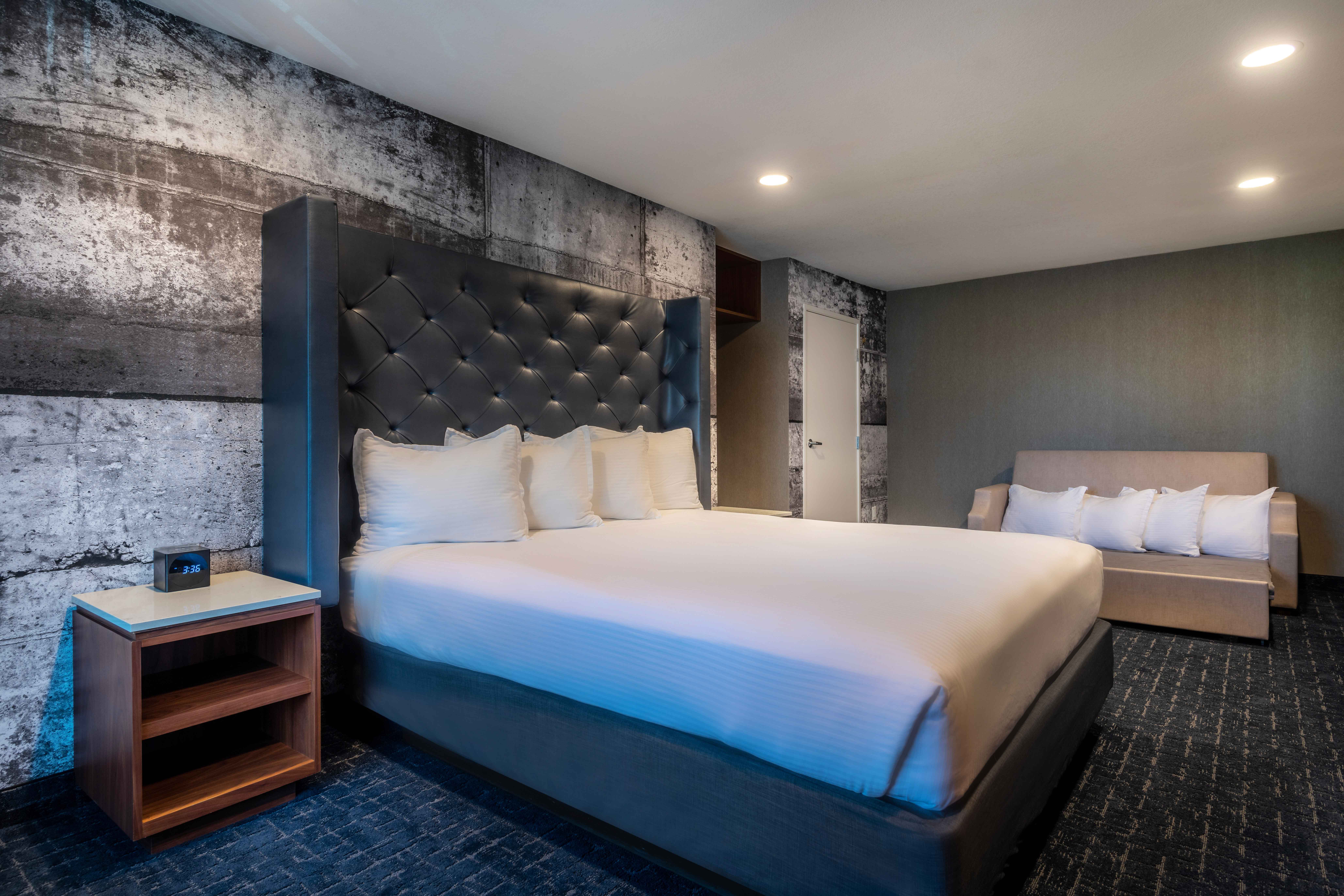 A hotel room with a king-sized bed, a sofa bed, and a nightstand.